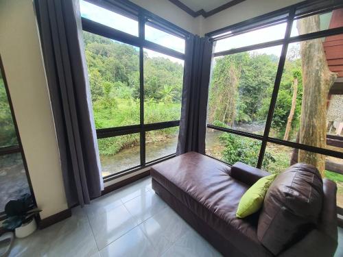 a living room with a couch and large windows at Malulee KhaoSok Resort in Khao Sok