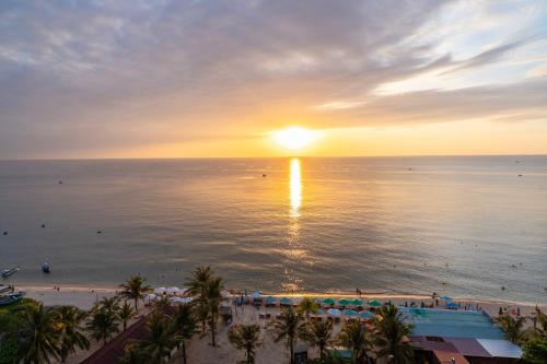 a sunset over the ocean and a beach with palm trees at Maris Beach Hotel Phu Quoc in Phu Quoc
