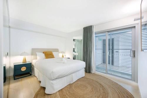 a white bedroom with a bed and a large window at Beach Front Urban 2 Bedrooms in Sydney