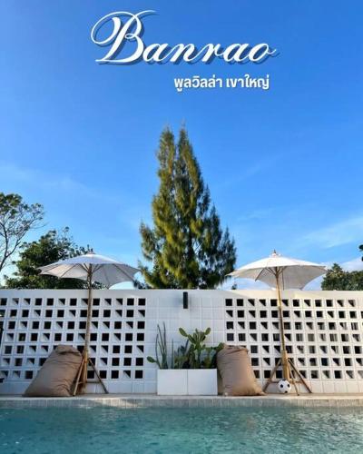 a pool with chairs and umbrellas next to a white fence at Banrao Pool Villa Khaoyai บ้านเราพูลวิลล่าเขาใหญ่ in Ban Tha Maprang