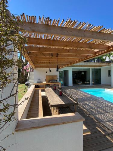 une terrasse en bois avec une table et une pergola en bois dans l'établissement Villa bord de mer avec piscine 200 métres plage, à Zonza