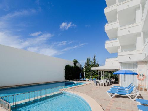 a pool with chairs and umbrellas next to a building at Apartamentos La Santa Maria in Cala Millor