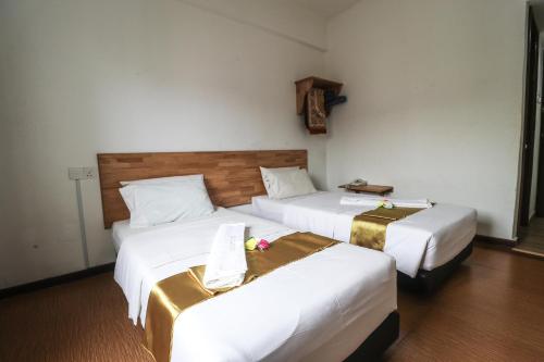 two beds in a hotel room with white sheets at AM Transit Inn Kuala Terengganu in Kuala Terengganu