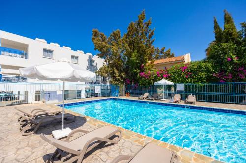 a swimming pool with chairs and umbrellas next to a building at Latchi Harbour Maisonette in Lachi