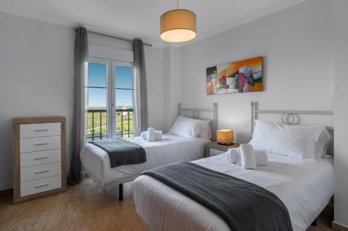 deux lits dans une chambre blanche avec une fenêtre dans l'établissement Las Marismas Atico PLUS by Ĥ - Isla Canela Golf GLHM59P19, à Isla Canela