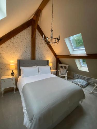 a bedroom with a large white bed with two windows at Cuckoo Penn Hideaway - Luxury Cotswold Retreat in Gloucestershire
