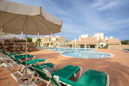 a group of lawn chairs and an umbrella next to a swimming pool at Glenridge By Albufeira Rental in Albufeira
