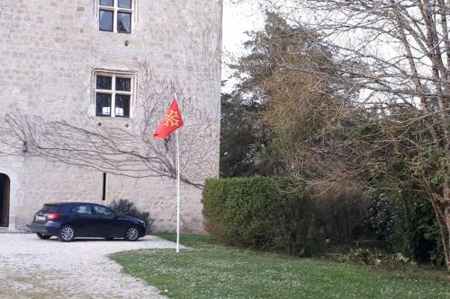 une voiture garée devant un bâtiment arborant un drapeau rouge dans l'établissement Château Tour du XIII siècle Gazaupouy, à Gazaupouy