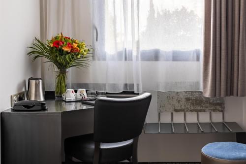 a desk with a vase of flowers and a chair at Best Western Saint Exupéry Eysines - Bordeaux Ouest in Eysines