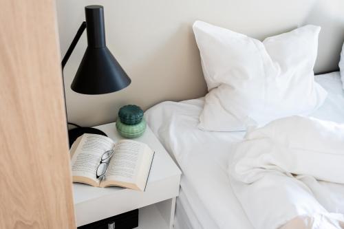 a bed with a nightstand with a book and a lamp at BJØRVIKA APARTMENTS, Opera Area, Oslo city center in Oslo