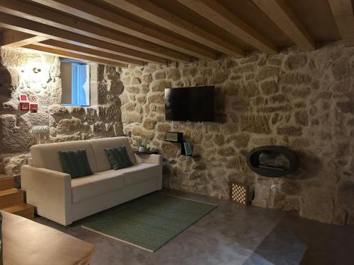 a living room with a couch and a tv on a stone wall at Story Studio Sortelha - Heritage in Sortelha