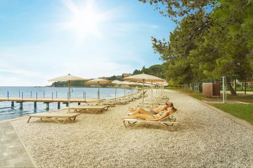 two women laying on chairs on a beach with umbrellas at Villas with Balcony or Terrace - Hotel & Resort Adria Ankaran in Ankaran