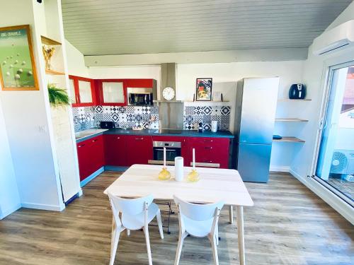 une cuisine avec des placards rouges, une table blanche et des chaises dans l'établissement Appartement Madiba face à la dune des Bourdaines !, à Seignosse