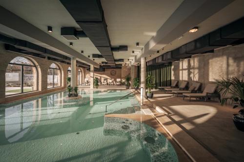 a large swimming pool in a building with tables and chairs at Bordűr Wellness Hotel Superior és Szőnyegmúzeum in Békésszentandrás