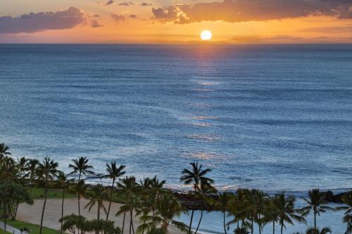 a sunset over the ocean with palm trees at Ko Olina Beach Villas O1404 in Kapolei
