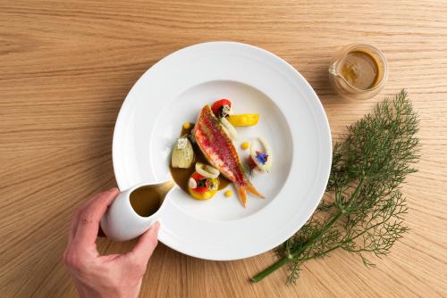 a person holding a white plate with food on a table at Althoff Hotel Villa Belrose in Saint-Tropez