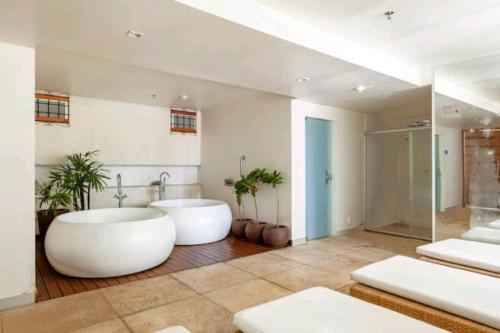 une grande salle de bains avec deux baignoires blanches et des plantes dans l'établissement Brisas do Lago em Brasília, à Brasilia