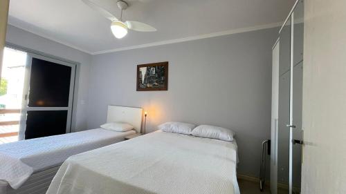 two beds in a white room with a window at Apto Centro Hospital Santa Cruz in Santa Cruz do Sul