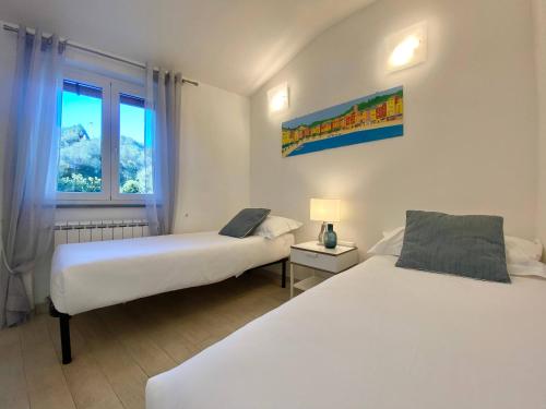 two beds in a white room with a window at ALLA CASA ROSA RAPALLO, Peaceful Multiple Apartment Surrounded by Greenery with Free Parking, WiFi & Air Conditioning in Rapallo