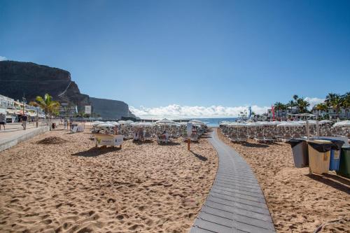 a sandy beach with chairs and umbrellas and the ocean at Apartamento Los Angeles 2 in Puerto de Mogán