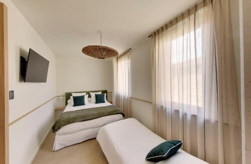 two beds in a room with a window at La Maison Gaïa Hôtel & Spa in Torreilles