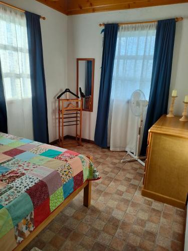 a bedroom with a bed and blue curtains and a fan at Casa da Matilde in Fajã de São João