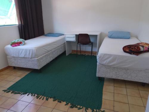 a room with two beds and a green rug at Hotel Pousada Liberdade in Pindamonhangaba
