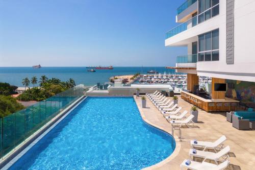 a swimming pool with chairs and the ocean in the background at AC Hotel By Marriott Santa Marta in Santa Marta