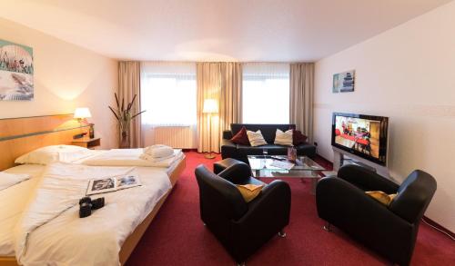 a hotel room with two beds and chairs and a tv at Hotel Deichgraf in Cuxhaven