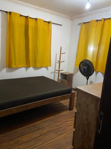 a room with a bed with yellow curtains and a fan at casa ilha de itamaraca in Itamaracá
