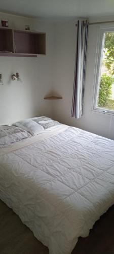 a white bed in a bedroom with a window at Mobil-home confort dans impasse boisée in Camiers