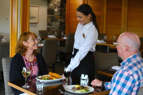 a waitress serving a man and woman at a table with food at Dunedin Leisure Lodge - Distinction in Dunedin