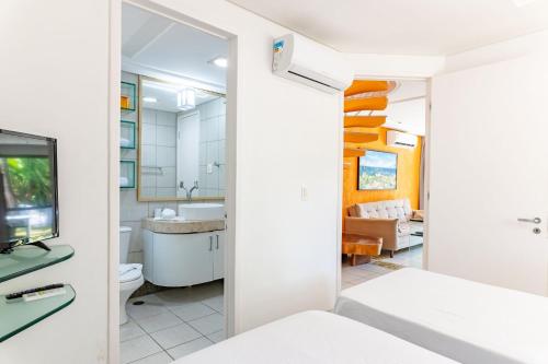 a bathroom with a toilet and a television and a living room at Flat ou Bangalo Luxo Beach Class Beira Mar Muro Alto in Porto De Galinhas