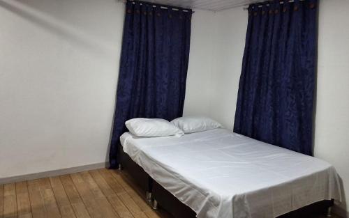 a small bedroom with a bed with blue curtains at Urantia Casa de la Montaña in Sutatausa