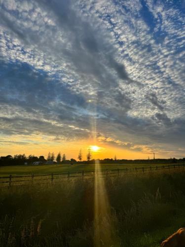 a sunset in a field with a fence and a sky at Field Farm Holiday Cottages and Glamping in Anderby