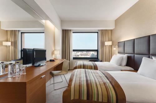 a hotel room with two beds and a desk with a television at Ramada by Wyndham Oradea in Oradea