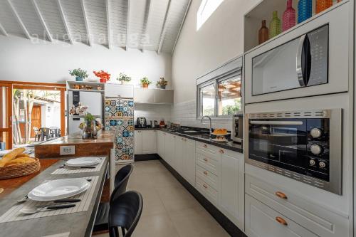 a kitchen with white cabinets and a table with chairs at Casa Luz do Verão - Com piscina na pinheira in Pinheira