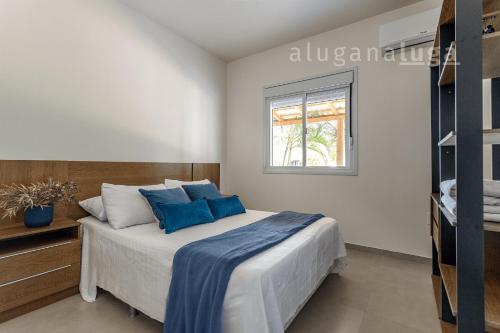a bedroom with a bed with blue pillows and a window at Casa Luz do Verão - Com piscina na pinheira in Pinheira