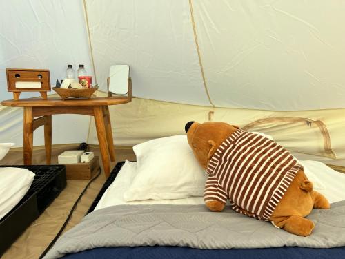 a teddy bear sitting on a bed with a pillow at บ้านไร่ไอดอย in Phrae