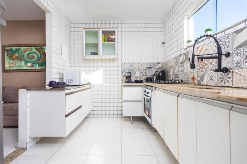 a white tiled kitchen with white cabinets and a sink at Refúgio Tropical Casa de Praia com Piscina Climatizada e 4 Suítes e garagem 3 carros, 800 mtrs da praia internet 700 mbps, condomínio privado com pista de skate , quadra de futevôlei , campos e quadras de futebol! in Cabo Frio