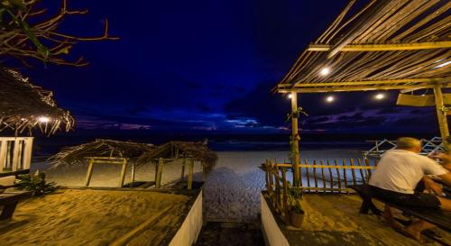 a man sitting on a bench looking at the ocean at night at Sea Shine Guest House in Hikkaduwa