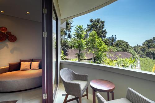 a room with a balcony with a couch and chairs at tanadewa Resort Ubud Bali by Cross Collection in Ubud