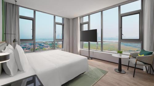 Un dormitorio con una gran cama blanca y grandes ventanales. en Holiday Inn Wuhan Houguan Lake by IHG, en Wuhan