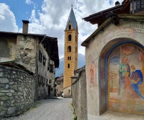 eine Kirche mit einem Glockenturm und einem Wandgemälde an einem Gebäude in der Unterkunft L'appartamentino del cuore in Bormio