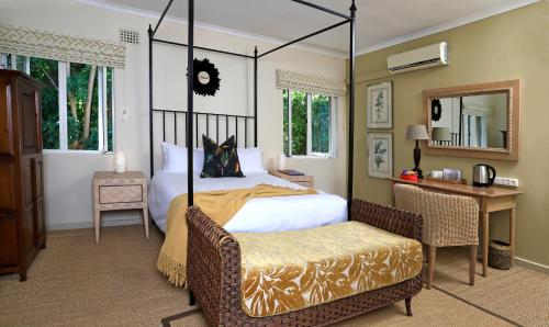 a bedroom with a canopy bed with a chair and a desk at Rosedene Guest House in Cape Town