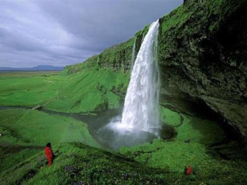 a waterfall on a hill with people standing in front of it at Prime Location-Golden Circle 3 Bedrooms in Selfoss