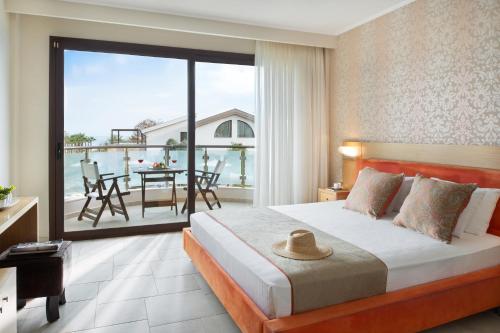 a bedroom with a bed and a balcony with a table at Alexandra Golden Boutique Hotel-Adults Only in Chrysi Ammoudia