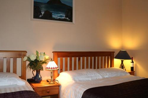 two beds in a bedroom with two lamps and flowers at An Portán Guest House in Dunquin