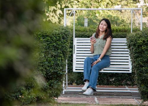 a woman sitting on a bench looking at her cell phone at Makan Resort in Kanchanaburi