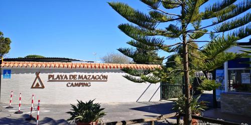 a building with a palm tree in front of it at Camping Playa Mazagón in Mazagón